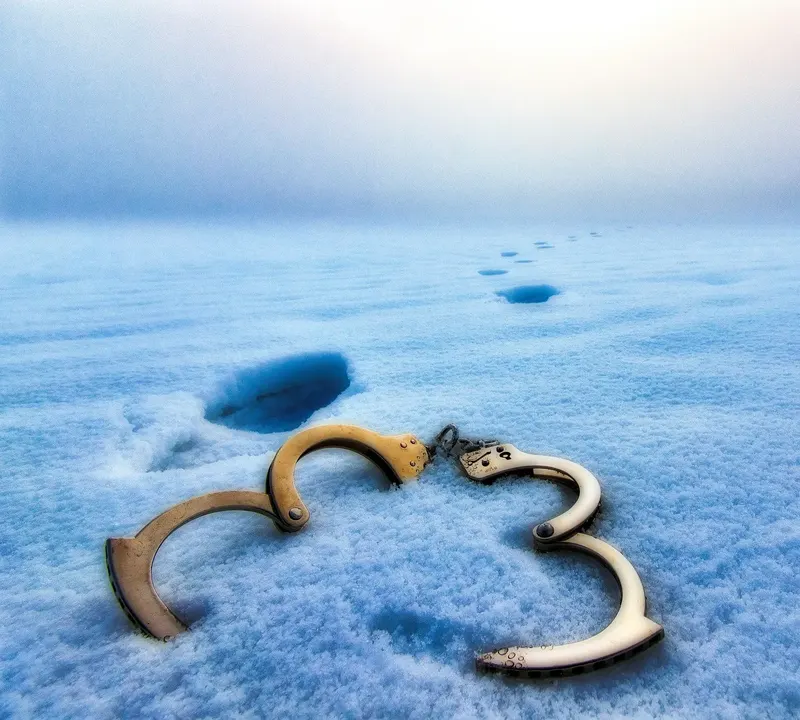 Geöffnete Handschellen im Schnee, daneben Fußspuren
